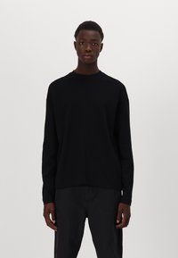 Schwarzes langärmliges T-Shirt aus Baumwolle mit Rundhalsausschnitt und relaxter Passform. Minimalistisches Design, keine sichtbaren Logos oder Muster.