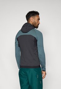 Kapucnis dzseki fekete törzzsel és türkiz ujjakkal, testhezálló kialakítással és eltérő textúrákkal. Funkcionális, praktikus kapucnival.