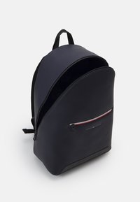 Zaino navy con un'esterno liscio, una tasca frontale con zip con accenti rossi e bianchi, e un manico superiore singolo. Interno scuro e spazioso.