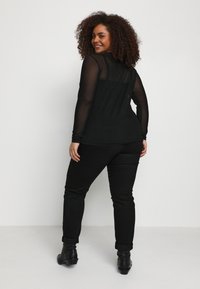 Black mesh long-sleeve top with polka dots, paired with black fitted pants, and ankle boots. The top features a sheer back design.