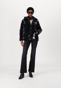 Black, glossy puffer jacket with a hood, geometric quilted pattern, front zip closure, and side pockets, paired with dark flared jeans and boots.
