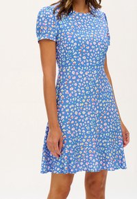 Kortärmad blå klänning med figursydd överdel och utsvängd kjol. Har ett flerfärgat djurmönster och en slät tygkvalitet.