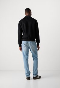 Black sweatshirt with a high collar, ribbed cuffs, and waistband, paired with light blue jeans and black sneakers with white stripes.