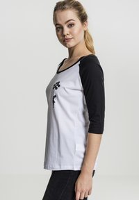 Driekwart mouw T-shirt, zwarte raglan mouwen, witte body, met een zwart grafisch ontwerp van een meisje met ballonnen op de borst.