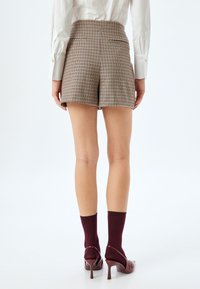 Hoge taille, bruine geruite shorts met twee achterzakken, gecombineerd met burgundy kousen en hakken, met een gladde textuur.