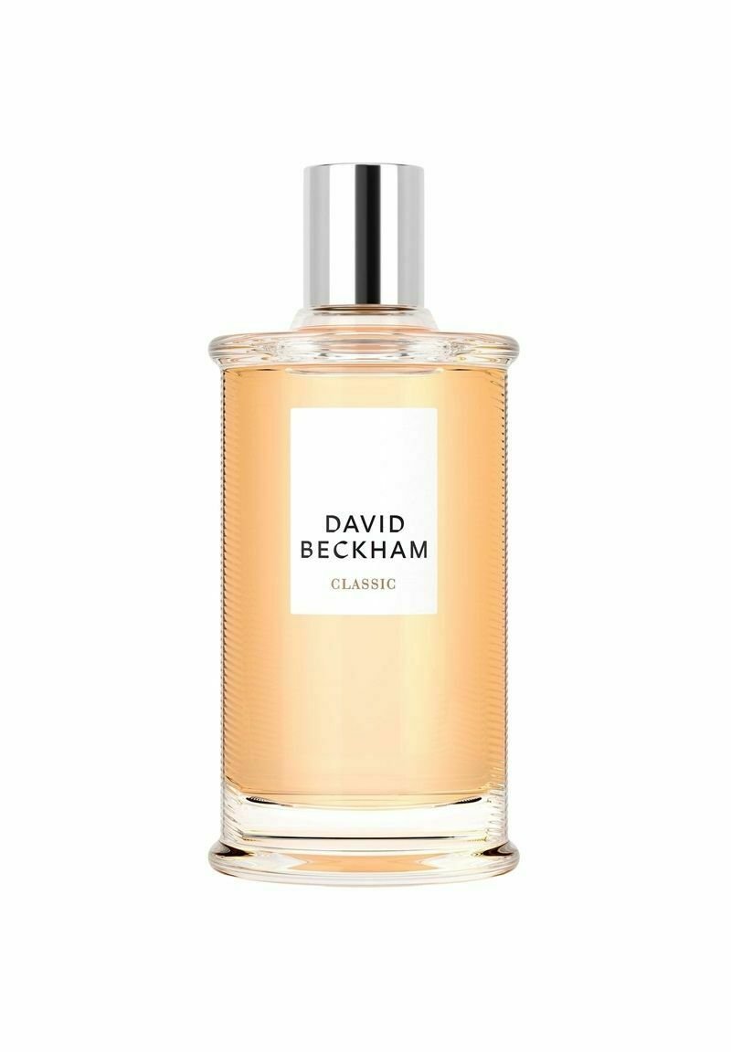 Genomskinlig glasparfymflaska med ribbad textur, silverlock och en vit etikett som visar "DAVID BECKHAM CLASSIC." Ljus bärnstenfärgade vätska inuti.