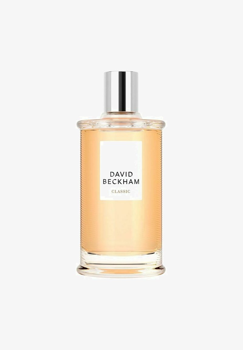 Klart glas parfume flaske med ribbet tekstur, sølvlåg og en hvid etiket, der viser "DAVID BECKHAM CLASSIC." Lys amberfarvet væske indeni.