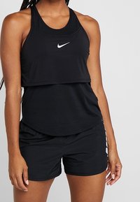 Sort atletisk tanktop med vandret ribbet tekstur og det ikoniske Nike-logo, parret med sorte shorts med sidelange striber.