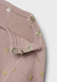 Tessuto a coste di un rosa chiaro con motivi a cuore glitterati dorati, dotato di automatici in metallo e di una piccola etichetta bianca nella zona del collo per una facile chiusura.