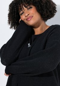 Cardigan noir en tricot avec des manches longues, présentant une coupe décontractée et un tissu texturé pour plus de détails. Aucun fermoir visible ni motifs.