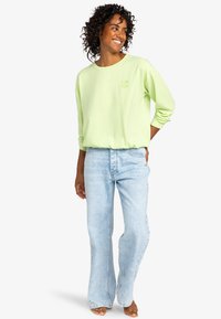 Light green sweatshirt with a round neckline, long sleeves, and embroidered flower detail. Paired with light blue flared jeans.