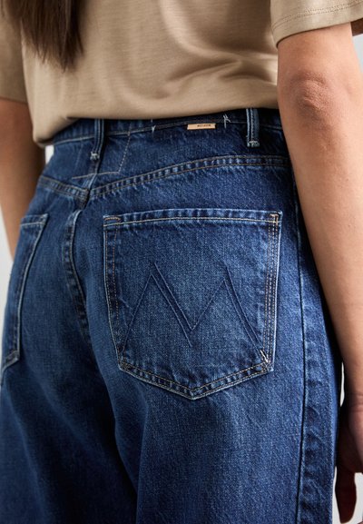 Donkerblauwe denim jeans met achterzakken voorzien van een chevron stitch patroon. Hoge taille met zichtbare stikseldetails.
