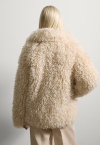 Beige Kunstfelljacke mit flauschiger Textur, oversized Passform und weiter Kragen. Die Rückenansicht zeigt ein weiches, voluminöses Design.