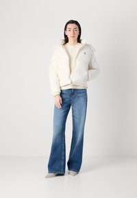 Kremfarget pufferjakke med cropped passform, glidelås, sidelommer og ribbede mansjetter, kombinert med lyseblå vide jeans.