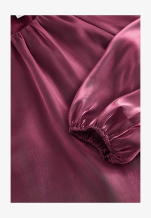 Vijolična satenasta bluza z gladko teksturo, nabranimi rokavi in nežnim leskom, z ohlapnim krojem in subtilnim padanjem.