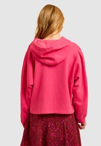 Roze hoodie met een cropped ontwerp, met een zachte binnenkant en brede mouwen. Draag het over een rok met bloemenpatroon.