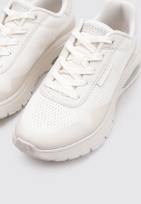 Une paire de chaussures de sport blanches Skechers avec un tissu en mailles, des semelles épaisses et un design à lacets sur un fond clair.