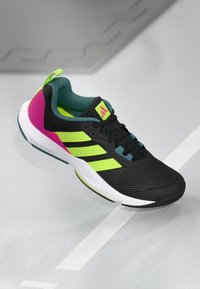 Black athletic shoe with textured surface, neon green and pink accents, three white stripes, and a white sole. Features a padded collar and laces.