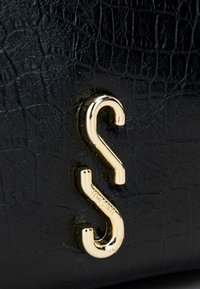 Borsa a tracolla in pelle nera con una texture a motivo coccodrillo. Presenta una chiusura a gancio in metallo dorato con un design curvo prominente.