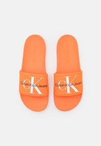Infradito arancioni con una fascia in tessuto che presenta il logo bianco "Calvin Klein Jeans" e un "CK" stilizzato. Suole testurizzate e flessibili.