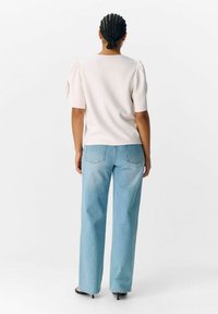 Lichtbeige pullover met korte pofmouwen, gecombineerd met hoge, losse blauwe jeans. Gladde textuur en minimalistisch ontwerp.