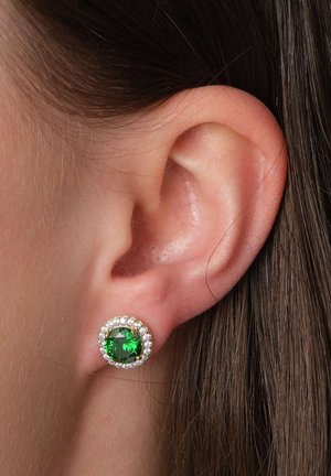 Close-up of ear wearing round stud earring with large green gemstone surrounded by small clear crystals.
