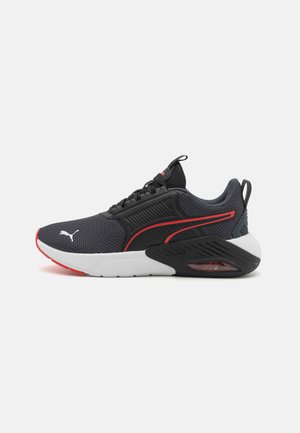 Sneakers Puma con una tomaia in mesh nero con accenti rossi, una suola intermedia bianca e un'unità d'aria visibile nel tallone. Pannelli laterali testurizzati visibili.