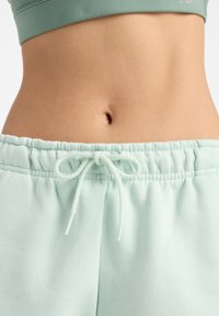 Pantalones de chándal suaves en verde menta, con cinturilla elástica y cordón ajustable. Tela suave con un corte holgado y detalles de costura.