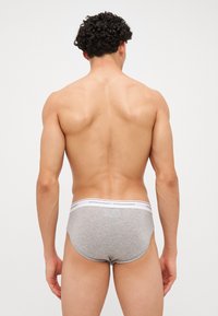 Bóxer de algodón gris con un diseño ajustado, que presenta una cinturilla blanca con la marca "DSQUARED2". Modelo mostrado desde atrás.