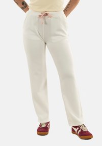 Pantalones de chándal blancos de corte holgado con cintura ajustable y un patrón rosa y blanco; estilo casual combinado con zapatillas rojas.