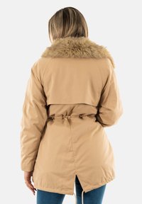 Parka marrone con collare in pelliccia sintetica, vita stretta e orlo con cordino. Presenta una vestibilità dritta, maniche lunghe e spacco laterale sul retro.