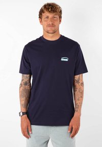 Camiseta de algodón azul marino con cuello redondo y mangas cortas, que presenta un pequeño logo azul claro en la parte izquierda del pecho.