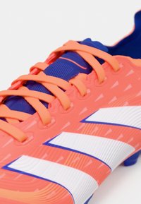 Scarpina da calcio di un vivace rosa con lacci arancioni e accenti blu. Presenta una superficie texturizzata e tre strisce bianche prominenti per il marchio.