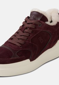 Bordowy zamszowy sneaker z miękką podszewką z polaru, zaokrąglonym noskiem, płaskimi sznurowadłami i kontrastową białą gumową podeszwą. Wytłaczane logo na języku.