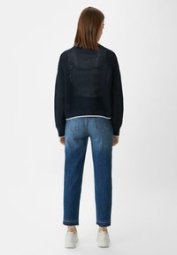 Marineblauer Strickpullover mit lockerer Passform und offenem Gewebe, kombiniert mit mitteldunklen, geraden Jeans und weißen Sneakers, zeigt einen lässigen Look.