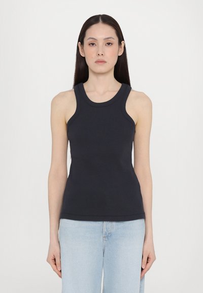 Camiseta sin mangas de color marino con un diseño ajustado, textura acanalada, agujeros amplios para los brazos y un escote redondeado, combinada con jeans de color azul claro.