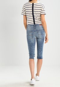 Camiseta de manga corta a rayas con detalle de botones en la espalda, combinada con pantalones capri de mezclilla azul. Zapatillas blancas completan el conjunto.