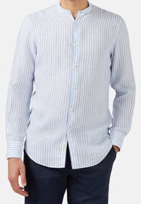 Jasnoniebieska i biała koszula na guziki w paski, z kołnierzykiem mandaryńskim, długimi rękawami i zaokrąglonym dołem. Materiał wydaje się lekki o teksturowanym wykończeniu.