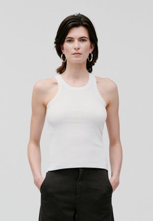 White cotton tank top with a racerback design and a fitted silhouette, paired with black trousers. Smooth texture, minimal detailing.