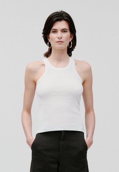 Biała bawełniana koszulka na ramiączkach z plecami w stylu racerback i dopasowanym krojem, zestawiona z czarnymi spodniami. Gładka textura, minimalne detale.