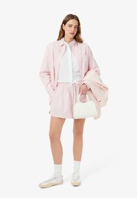 Camicia a righe rosa e pantaloni corti abbinati, camicia bianca a maniche lunghe sotto, abbinata a una giacca rosa chiaro e una piccola borsa bianca.