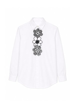 Wit overhemd met lange mouwen, knopen en kraag, versierd met drie grote zwart-witte geborduurde bloemen in het midden voor.