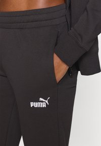 Μαύρο παντελόνι φόρμας από απαλό ύφασμα, με ελαστική μέση, πλαϊνές τσέπες και λευκό λογότυπο Puma στο αριστερό πόδι.