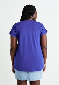 Purple short-sleeve top with a relaxed fit, soft texture, and a curved hem, paired with a light blue denim skirt.