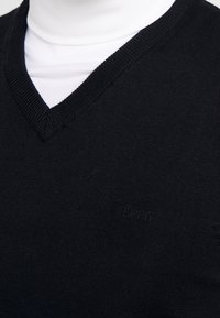Schwarzer Strickpullover mit V-Ausschnitt. Verfügt über gerippte Kanten und ein dezentes "Esprit"-Logo auf der Vorderseite. Glatte Textur, eng anliegendes Design.