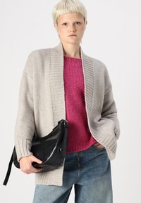 Lys grå strikket cardigan med ribbestrikket tekstur, båret over en lys rosa genser. Svart skinn crossover-veske med justerbar stropp. Denim jeans.