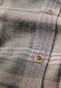 Camisa de lino con un patrón de cuadros azul y blanco, que presenta un botón hecho de un material claro, mostrando una superficie texturizada.
