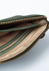 Groene ritstas met een gestructureerde buitenkant. Interieur voorzien van een beige voering en meerdere kaartsleuven. Gouden ritsbeslag.