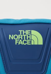 Mochila azul com superfície texturizada, apresentando um logo verde da "The North Face" e um design de acento curvado na parte superior.