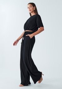 Černý dvoudílný outfit složený z krátkého topu s krátkým rukávem a širokými kalhotami. Texturovaná látka s kapsami a stažitelným pasem.